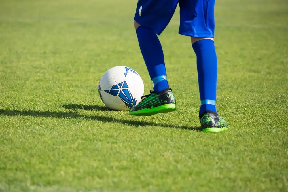 Young soccer player in blue socks and green cleats dribbling a ball on grass