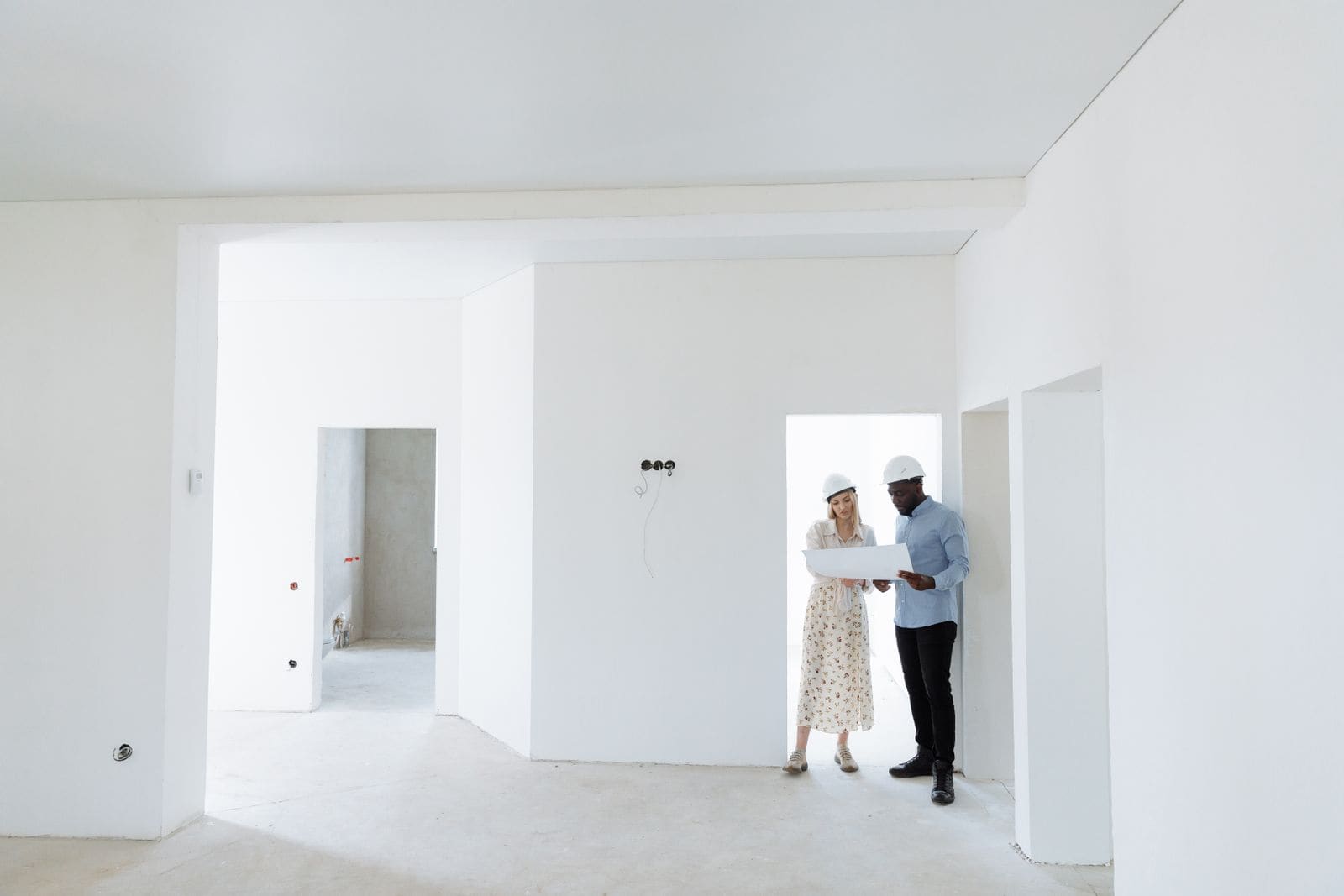Two people in white hard hats review a plan inside an unfinished home
