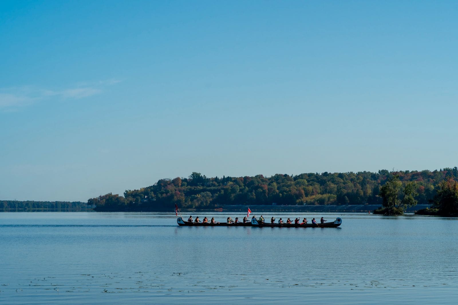 Large canoe crew paddling together across a calm lake