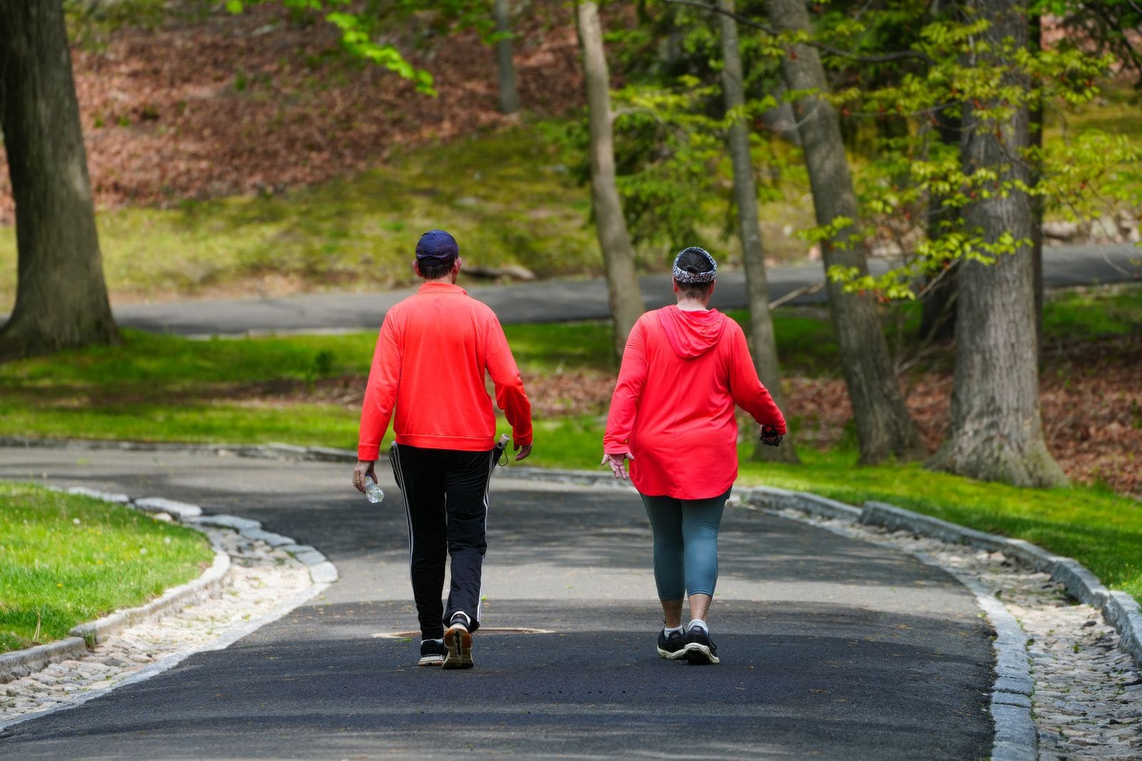 Two people in red tops walking briskly along a paved park path