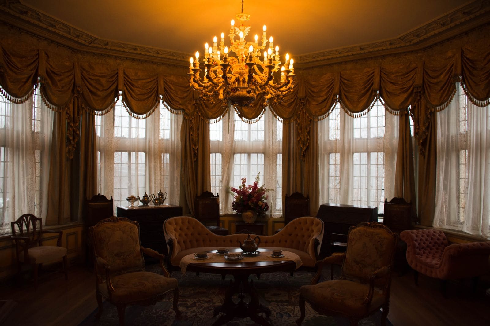 Victorian parlour with a lit chandelier, tufted sofa and a tea set